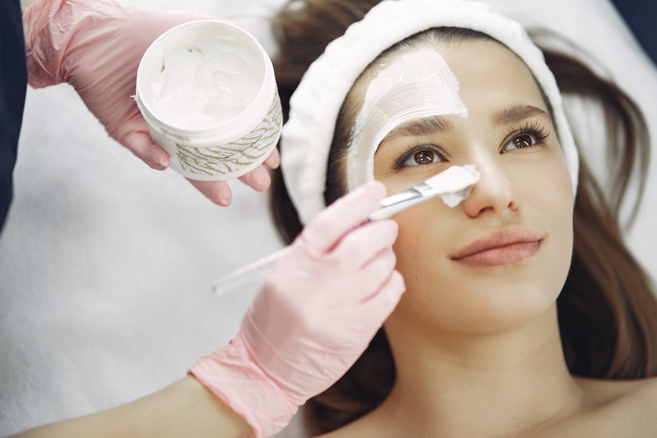 Close-up of a woman receiving a facial treatment at a spa with a cream mask applied using a brush.